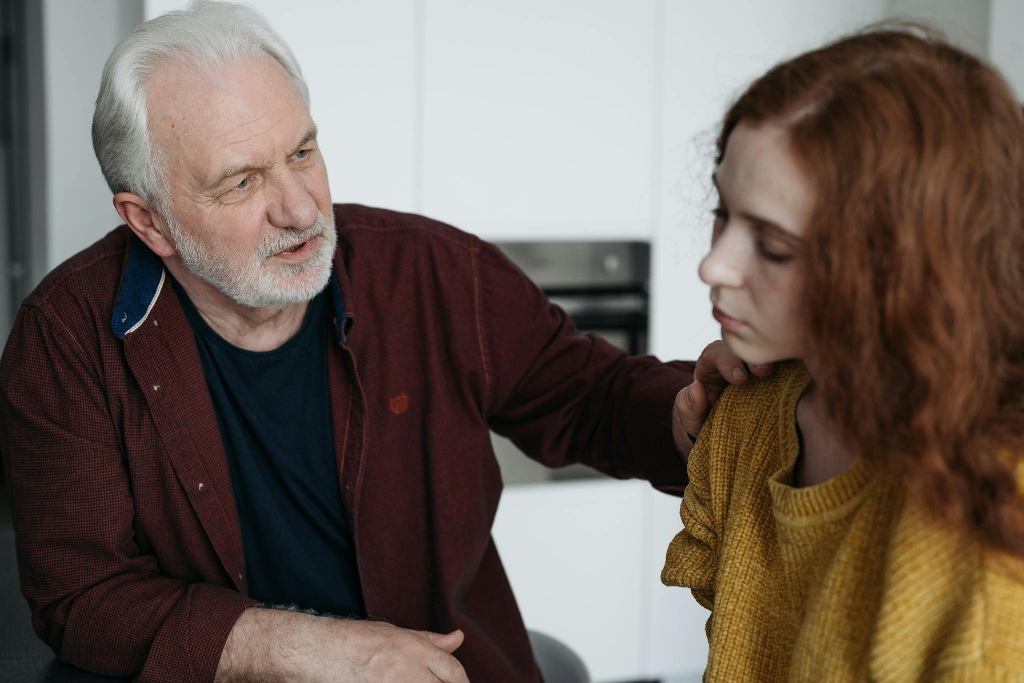 An elderly man consoles a young woman indoors, expressing empathy and understanding.